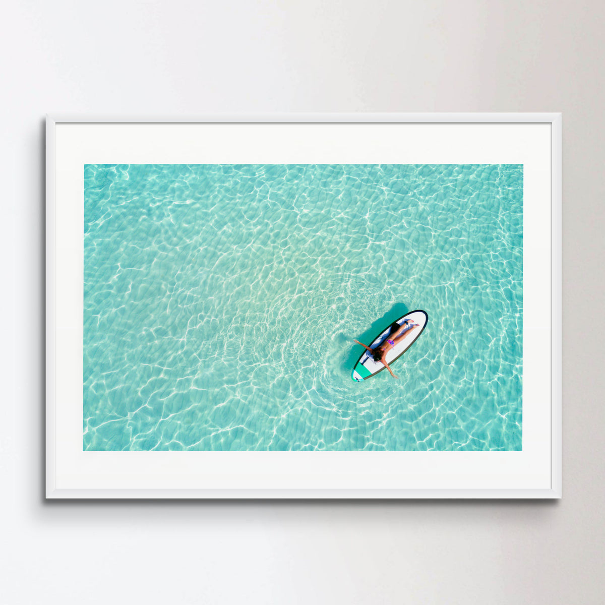 Aerial view of a woman on a surfboard in the turquoise waters