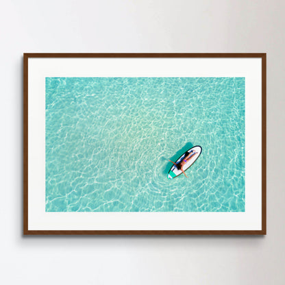 Aerial view of a woman on a surfboard in the turquoise waters
